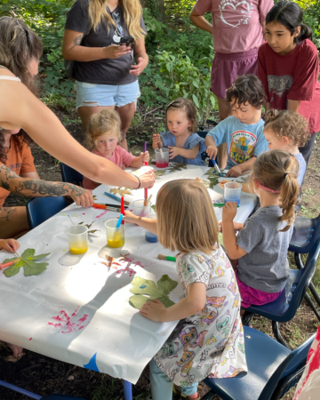 toddlers painting with assistance from adults on a canvas stretched over a table