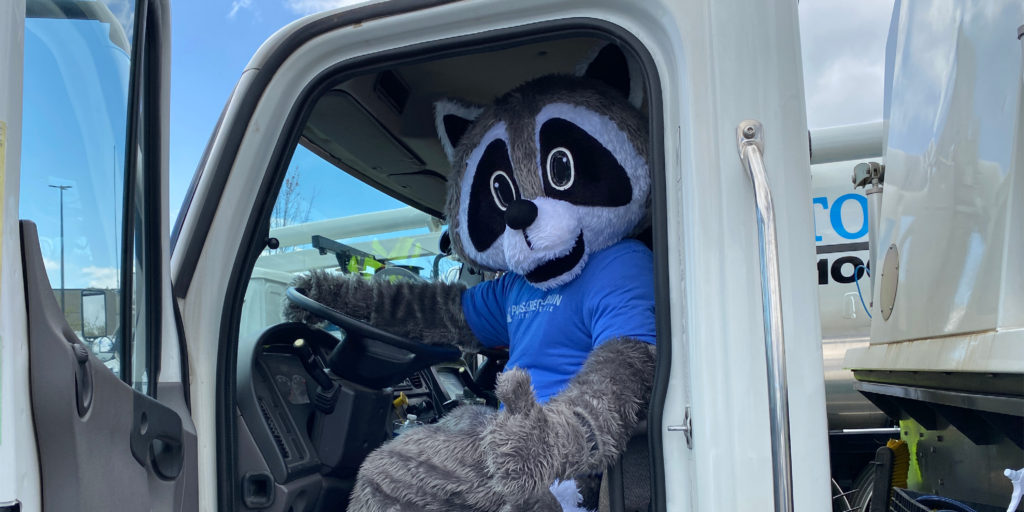 adult in raccoon mascot costume at steering wheel of oversized vehicle