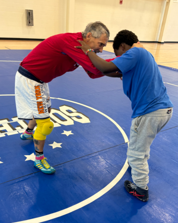 adult teaching child how to wrestle on wrestling mat