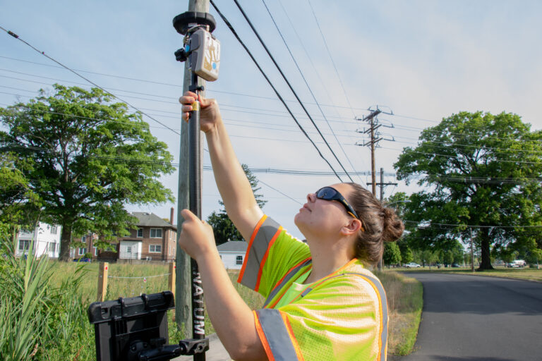 A worker in a high-visibility vest uses specialized equipment to take readings as part of a stormwater system survey.