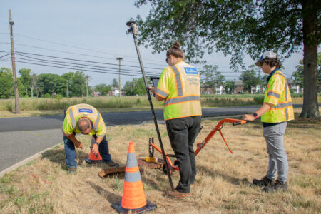 Workers in yellow high-visibility vests use specialized equipment to survey stormwater infrastructure.