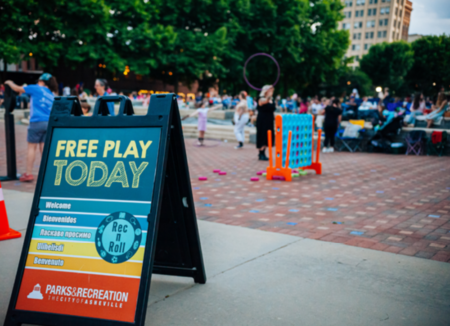 a-frame sign welcoming community members to play area with lawn games and hula hoops