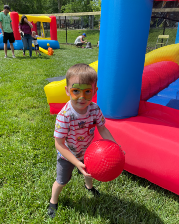 kid holding a kickball in front of a bounce house