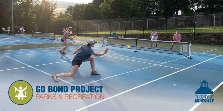adults playing doubles pickleball while others watch