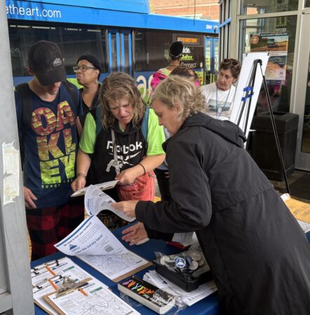 riders at a table looking at paper surveys and maps and talking with volunteers during a survey event on May 26, 2026.