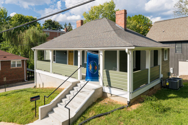 restored green house on hill with blue banner flag off porch