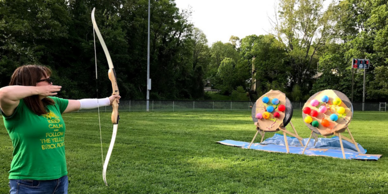 adult aiming archery crossbow at balloons on a target