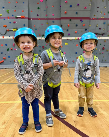 kids in climbing helmets in front of an indoor climbing wall